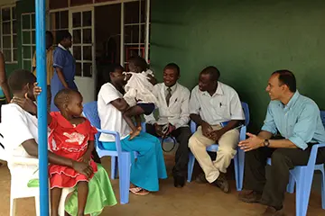 Doctors from the global health group sitting in chairs outside of a clinic chatting with patients