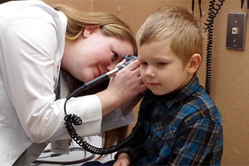 Doctor examining the right ear of a young male patient in an exam room