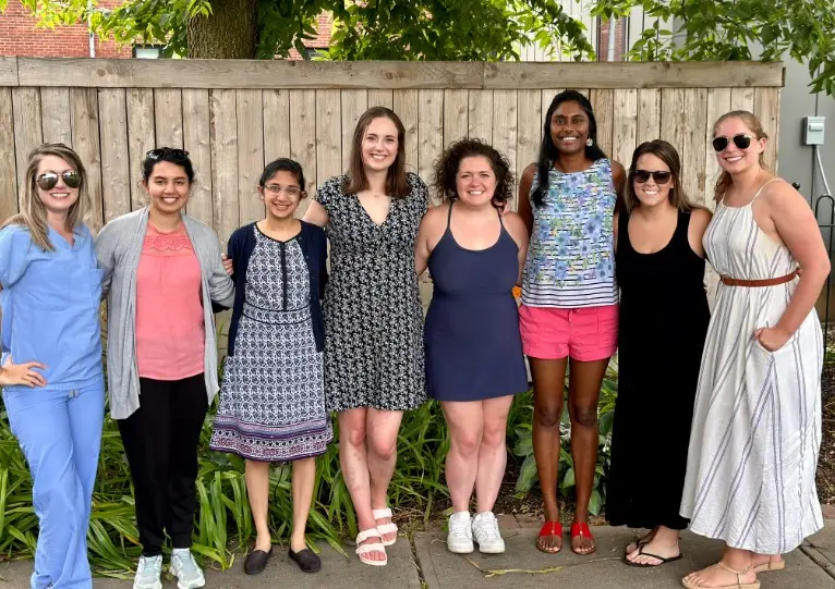Photo of 9 fellows together in front of a wooden fence