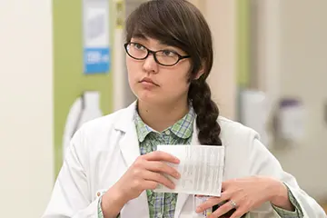 Person in a lab coat carrying notes