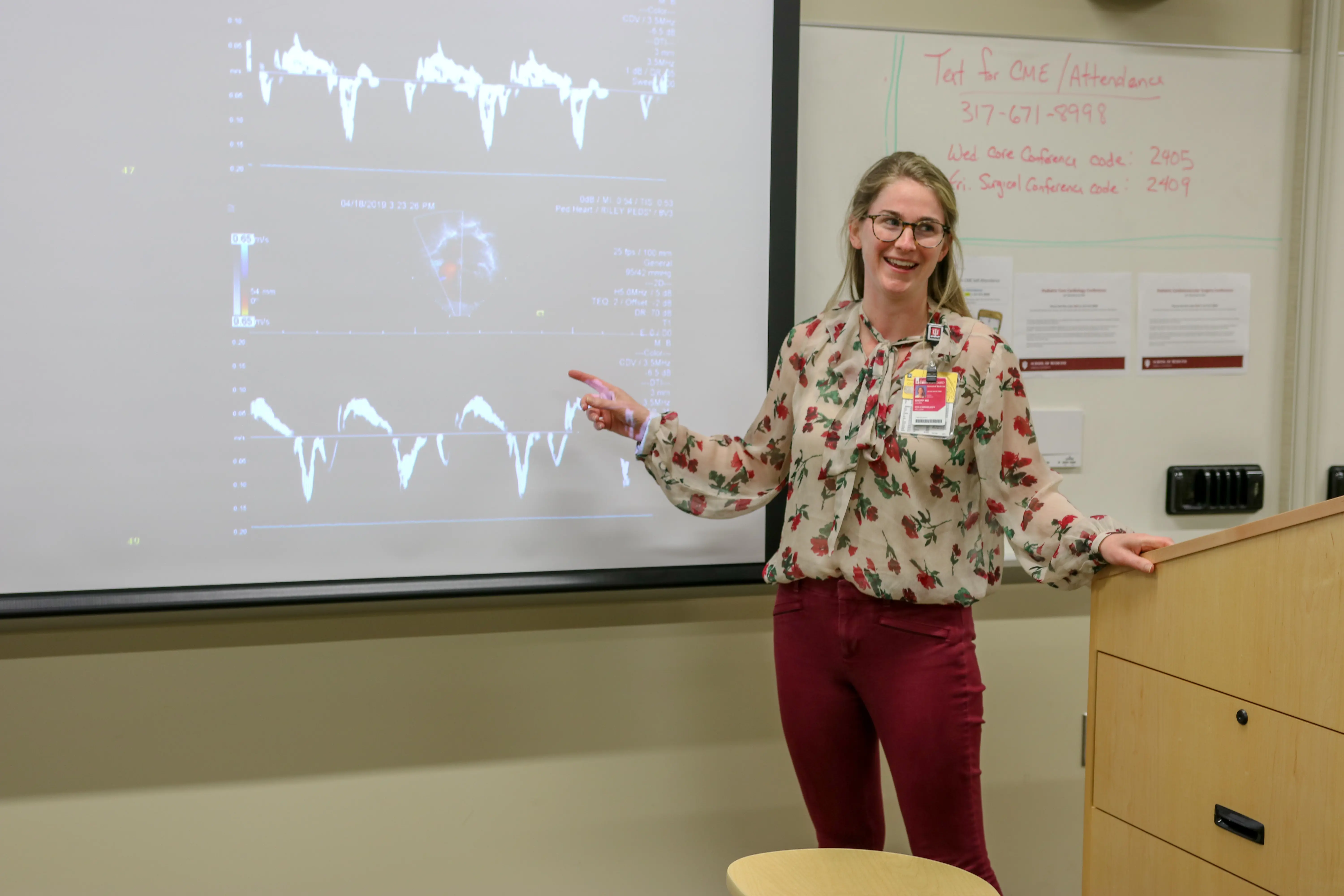 A woman points to data on a projection at the front of a classroom