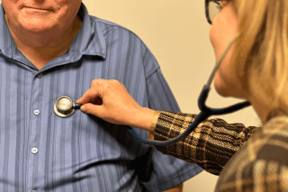 a physician listens to a patient's heart with a stethoscope