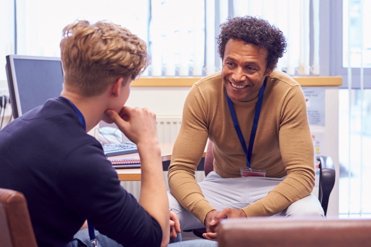 a pyschiatrist smiles while speaking with a young patient in his office