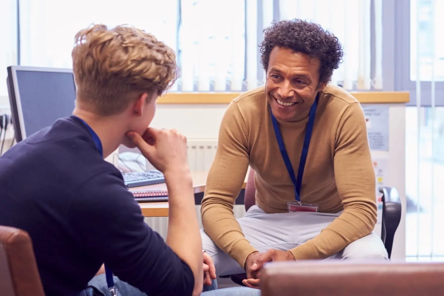 a pyschiatrist smiles while speaking with a young patient in his office