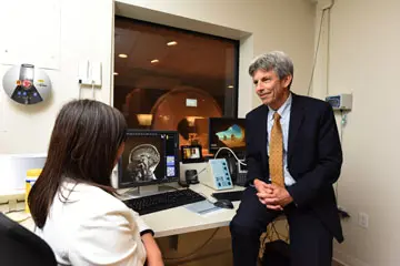 Two researchers talking, one sitting in chair and the other leaning on table 