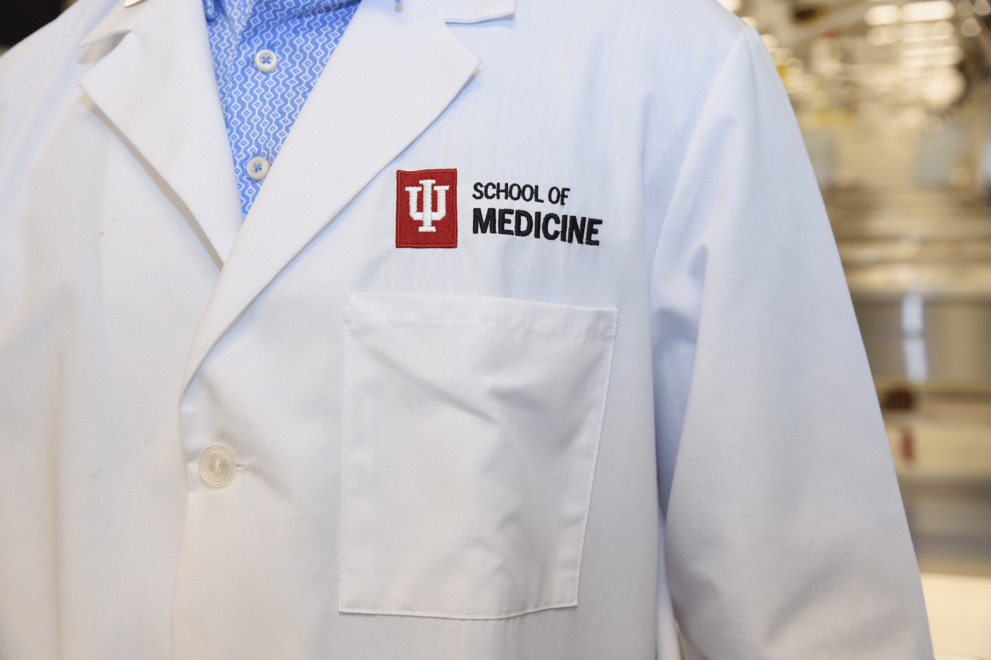 A trainee wearing a blue-patterned button up with an IU School of Medicine white coat.