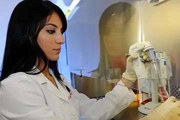a researcher in a white coat prepares a research sample under the lab's safety hood