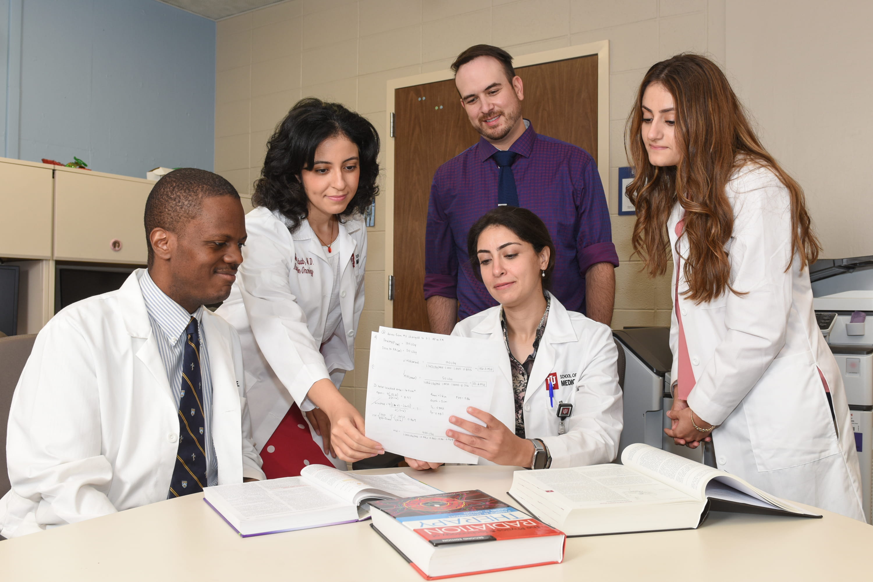 five Radiation Oncology residents looking over a document together 