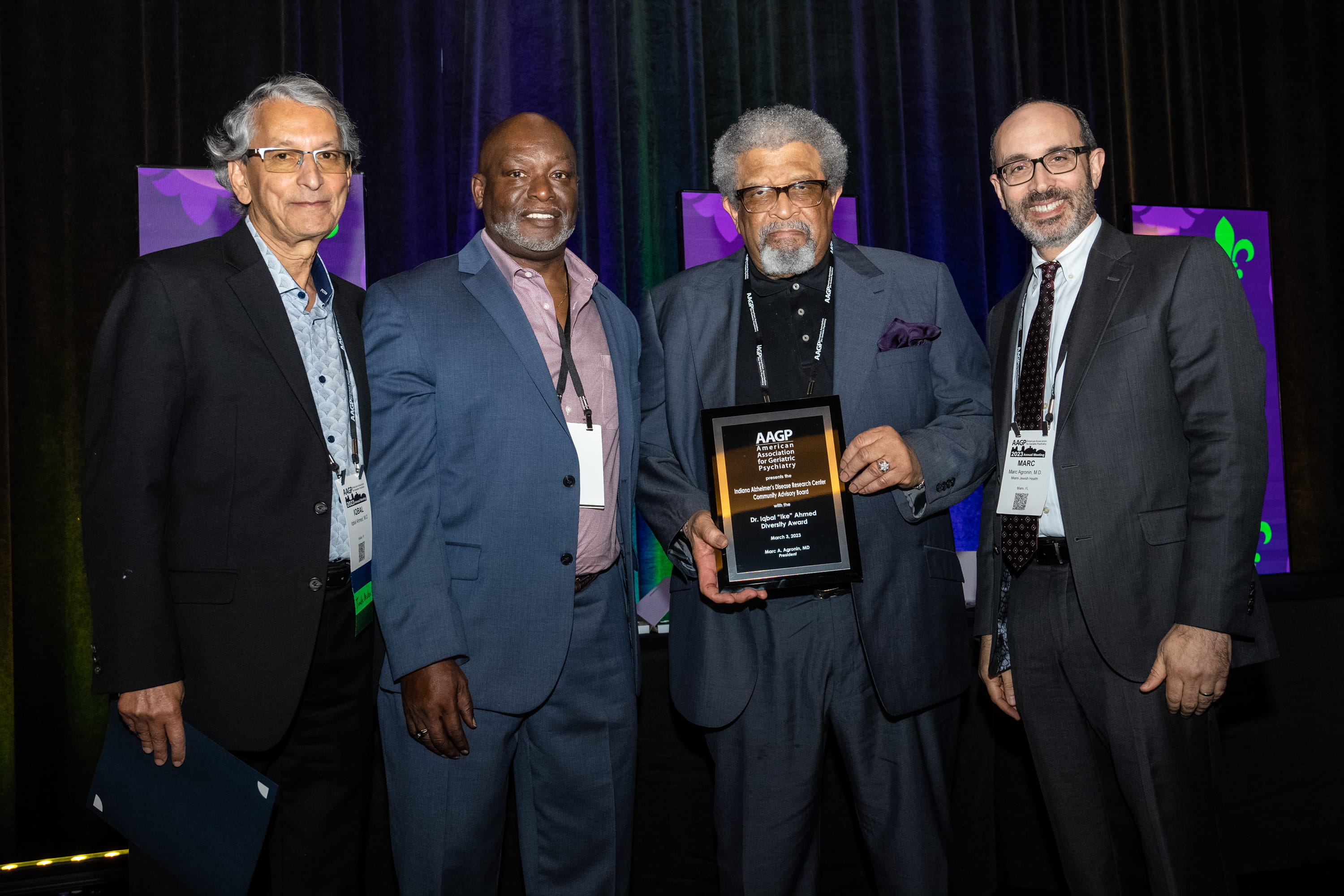 four people stand together, one holding an award