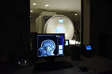 A brain scan is displayed on a monitor. An MRI machine sits in the background.