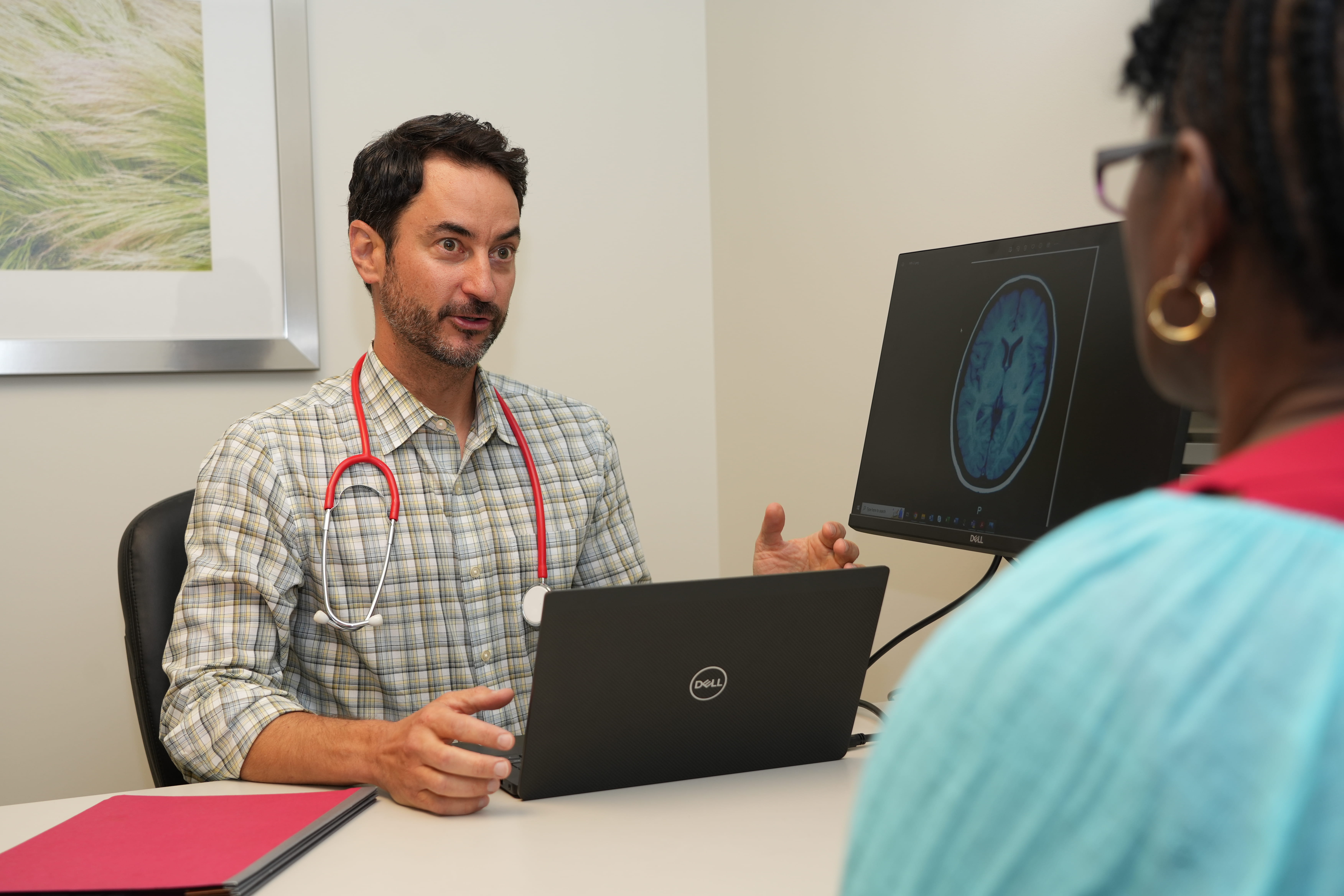 A male physician speaks with a female patient, explaining her MRI scan results.