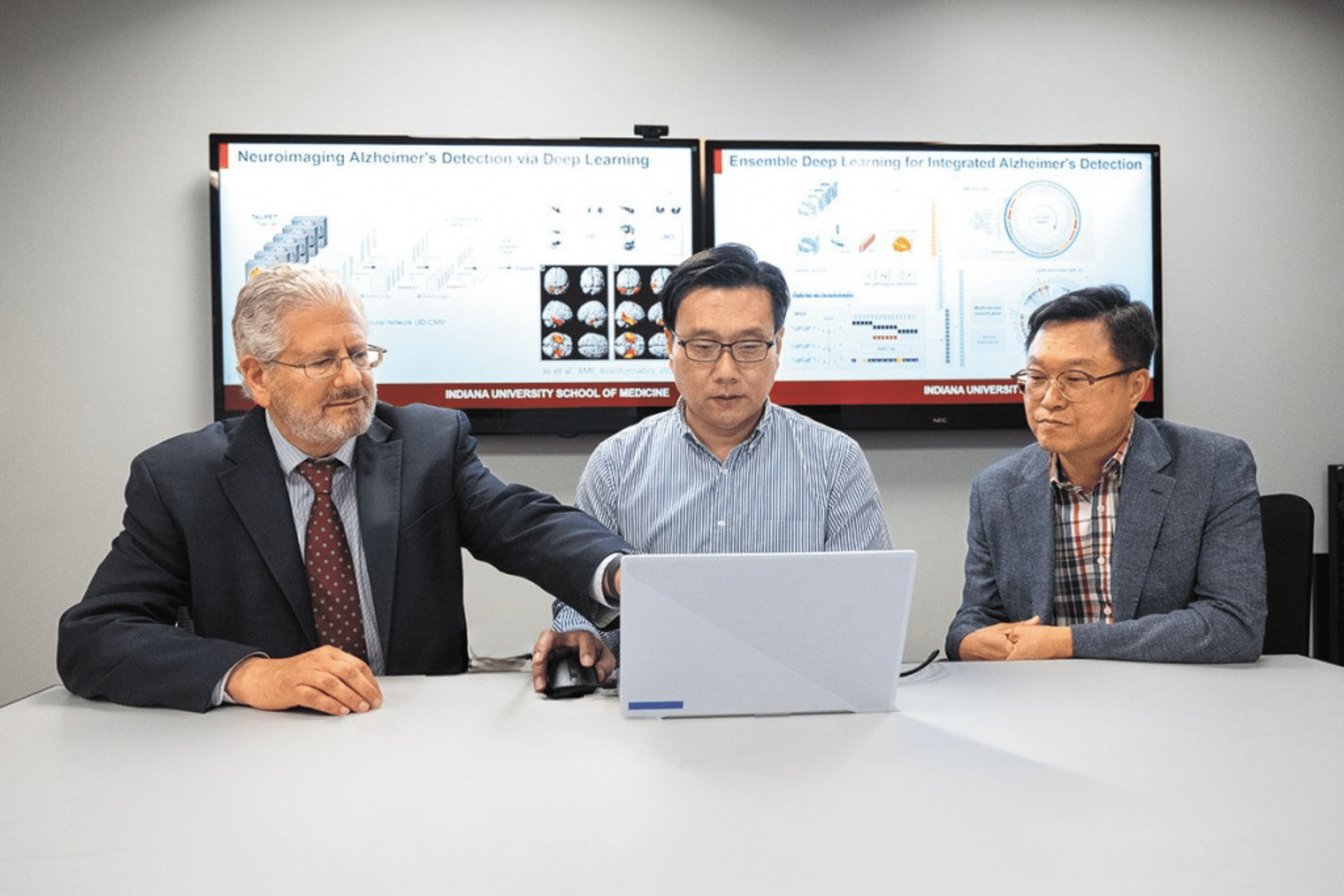Three male scientists collaborate on a project on a laptop.