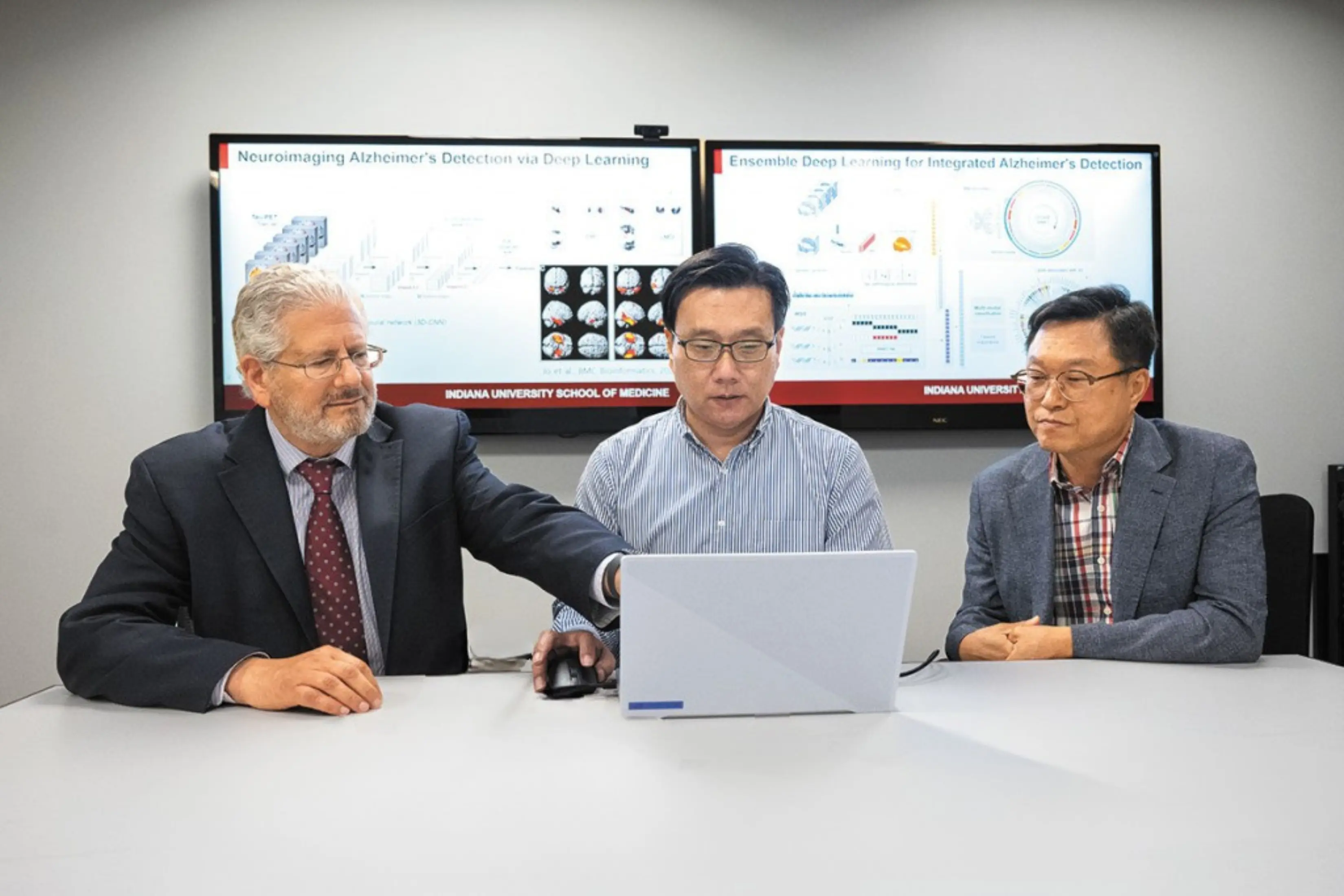 Three male scientists collaborate on a project on a laptop.