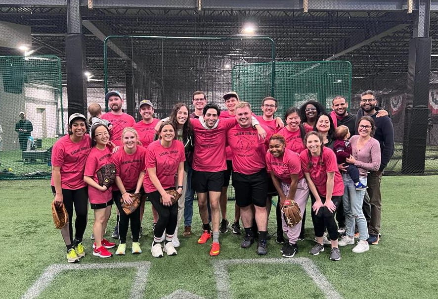 Picture of Dept of Surgery Residents in their softball uniforms huddled together smiling