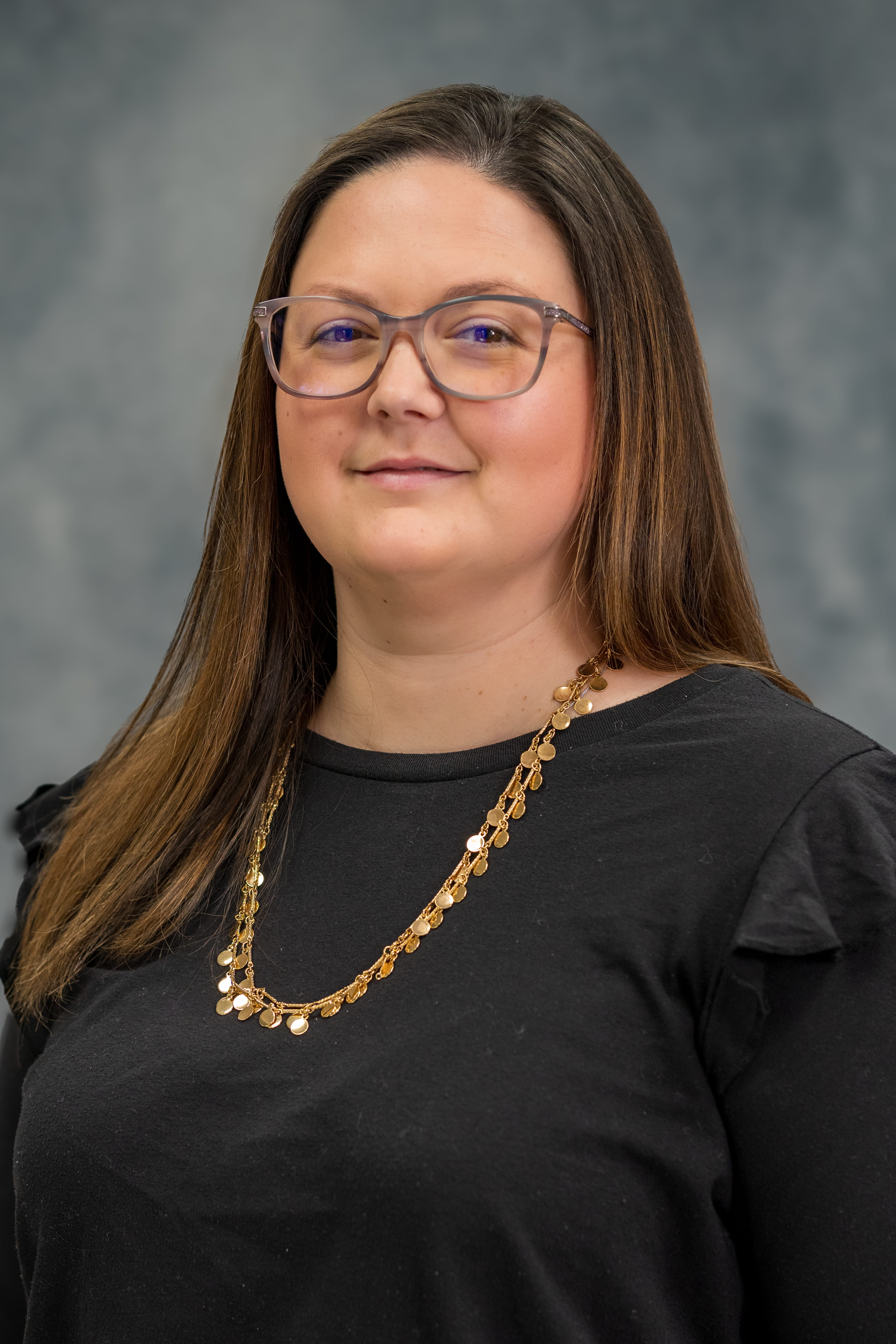 Professional headshot of a Caucasian female, dark brown hair and wearing a black blouse. background is a dark mottled grey