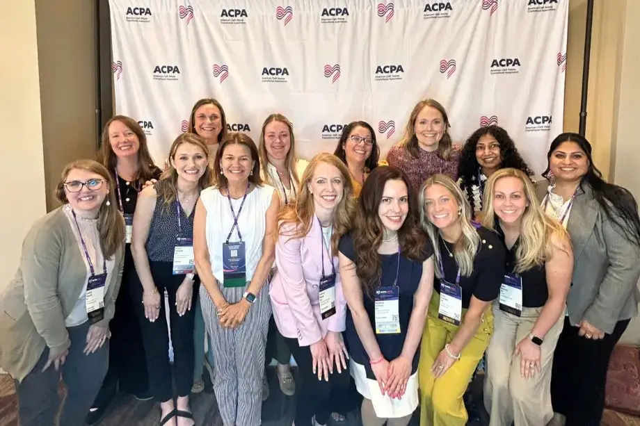 Group of 12 women stand in front of an ACPA backdrop posing. All are wearing business casual clothing and of varying ethnicities.