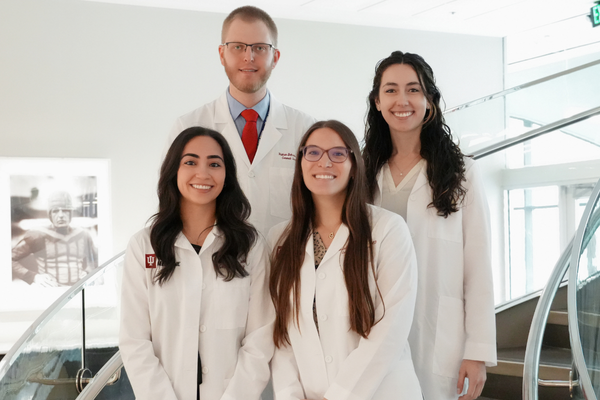 IU RISE surgical education fellows clockwise from top left; Nathan Behren, MD, Maya Hunt, MD, Noosha Deravi, MD, and Brielle Warnock,MD in the white coats standing ona  staircase.