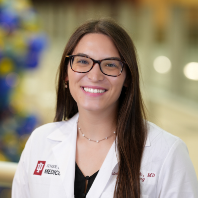 Portrait of Brielle Warnock, MD, MS, smiling and wearing glasses and a white medical coat, against a softly blurred background.