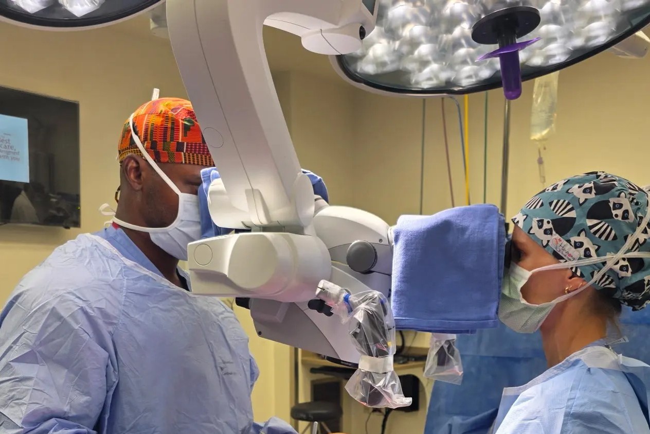 One male and one female surgeon look through an enhanced loupe to perform a microsurgery on a paitnet. 