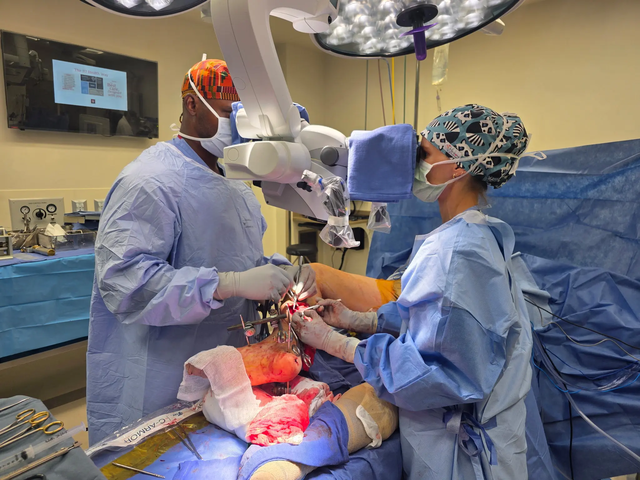 One male and one female surgeon look through an enhanced loupe to perform a microsurgery on a paitnet. 