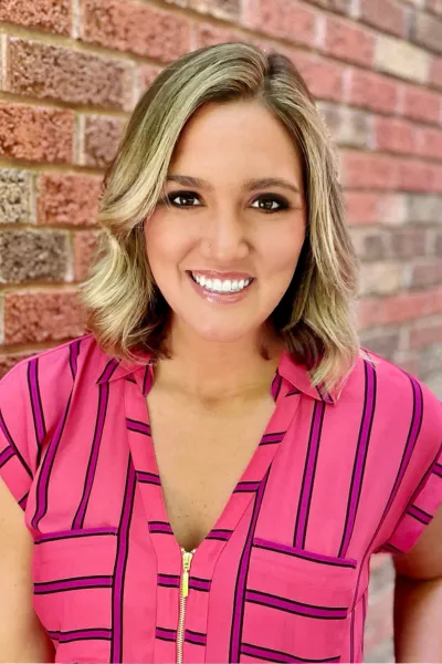 Professional headshot of Emily Skoniecke in a pink and purple top on a brick background