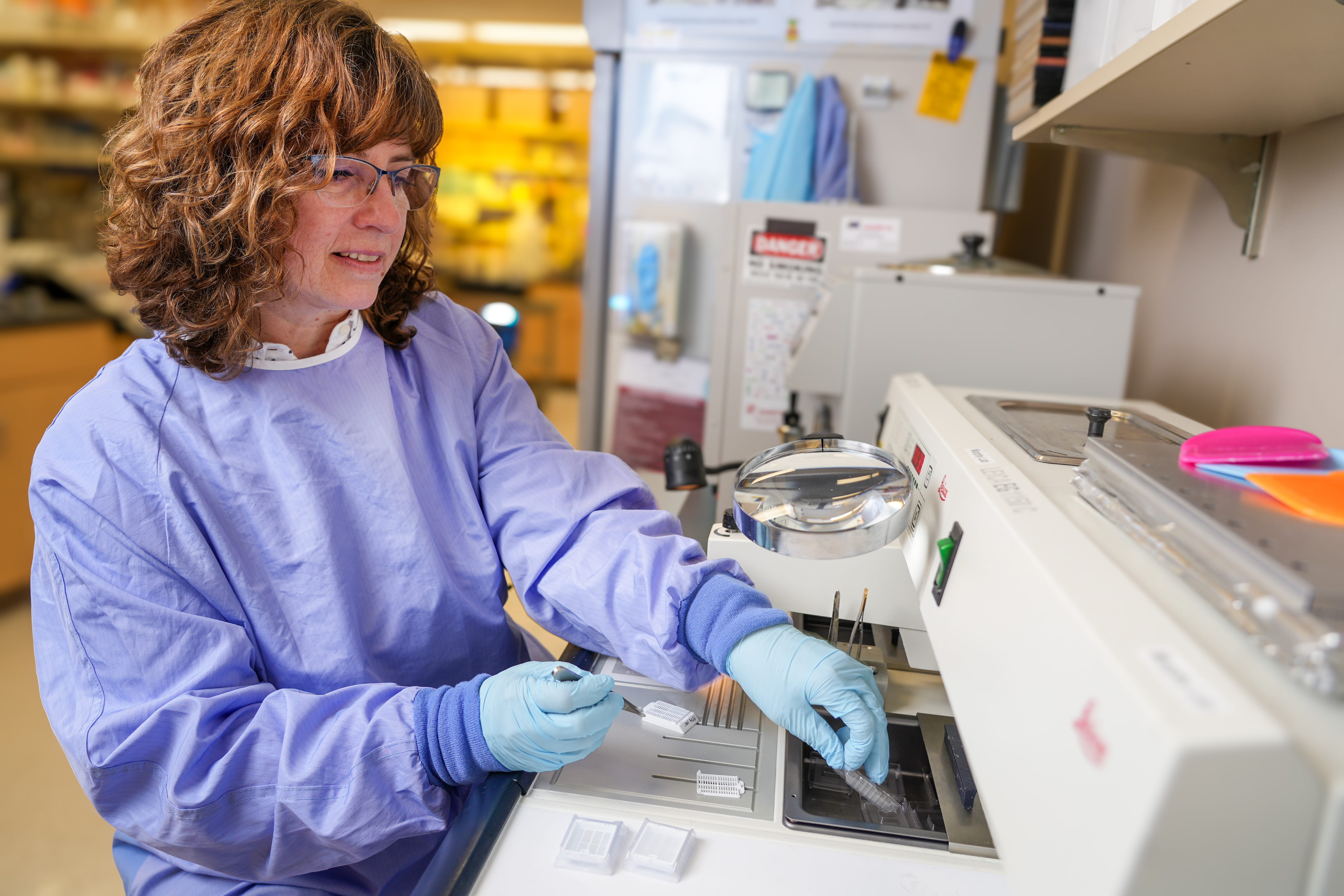 Jennifer Stashevsky, wearing a protective gown and gloves, prepares a sample at the paraffin machine in the Murphy lab.