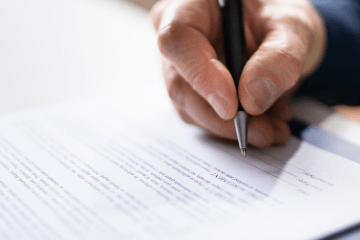 Image of a caucasian hand with a pen getting ready to sign an agreement