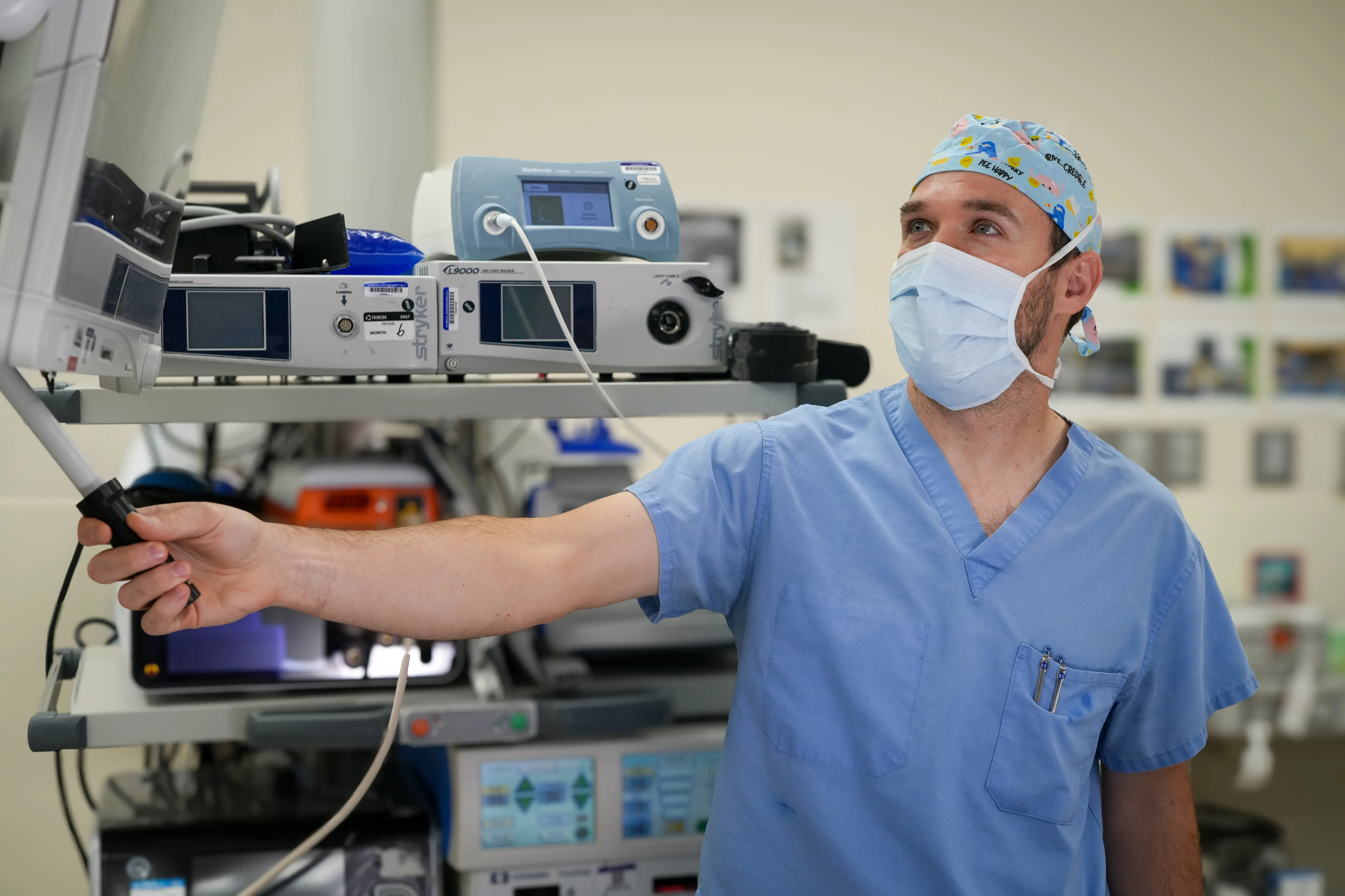 A medical professional in blue scrubs operates surgical equipment in a hospital operating room.