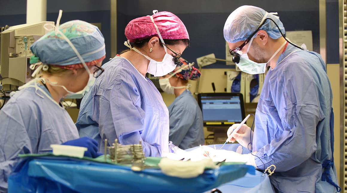 three surgeons in scrubs and caps work together in the operating room
