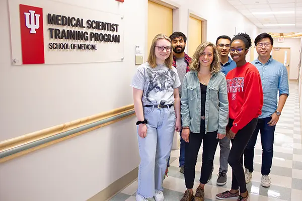 Group of 6 MSTP students standing near the IU Medical Scientist Training Program sign in a hallway