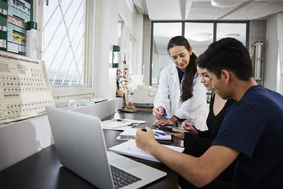 an educator looks over the shoulder of a student working on a laptop