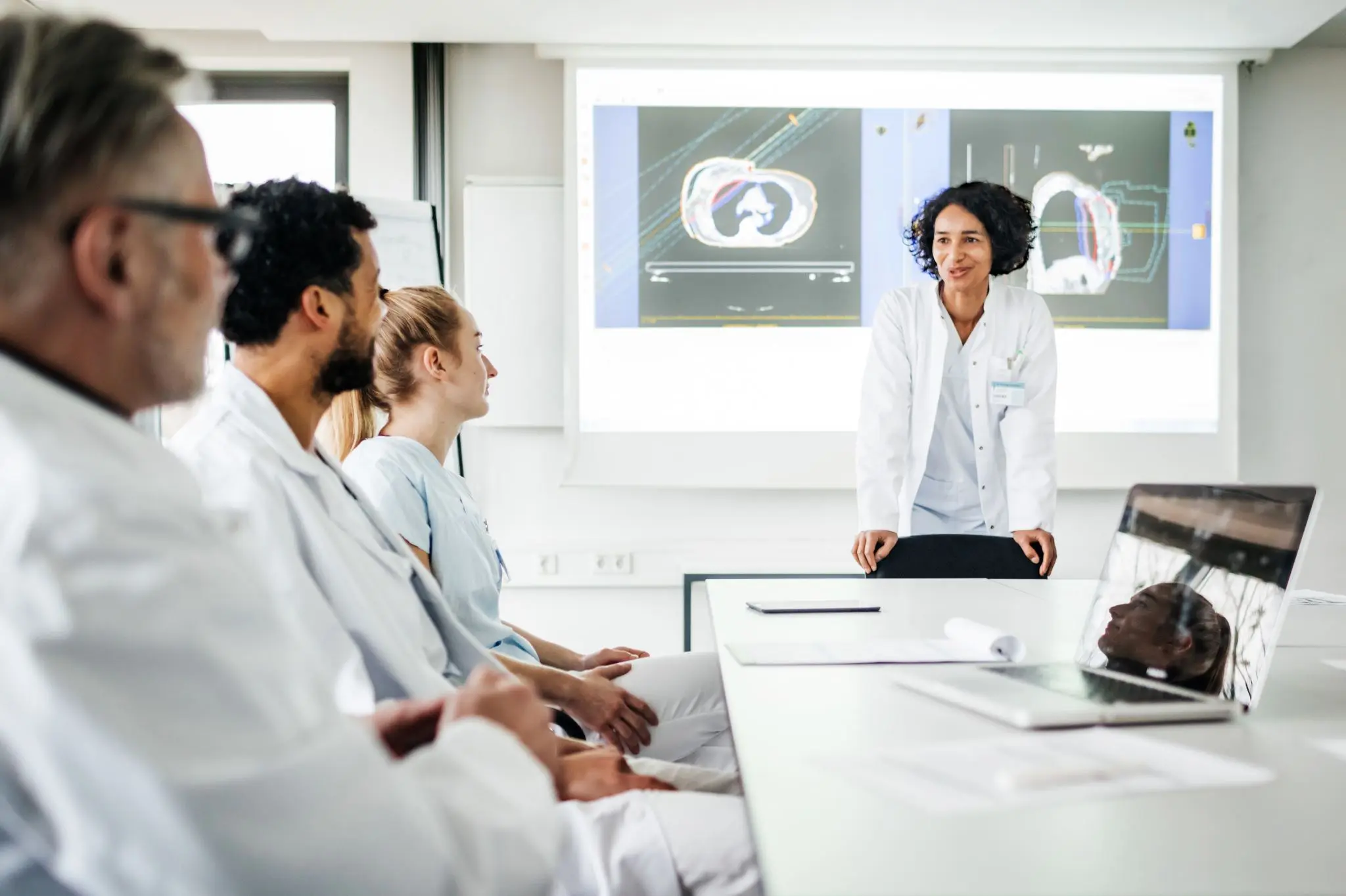 clinical leaders meet around a table with slides projected in the room behind them