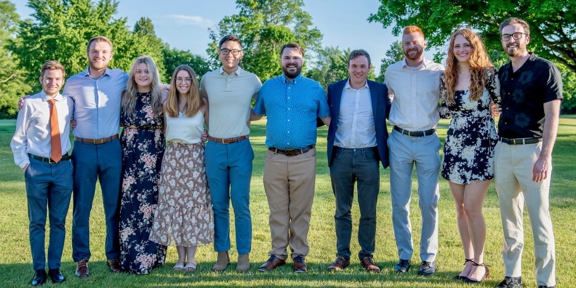 ten residents stand outside on a sunny summer day in nice clothes with their arms around each other