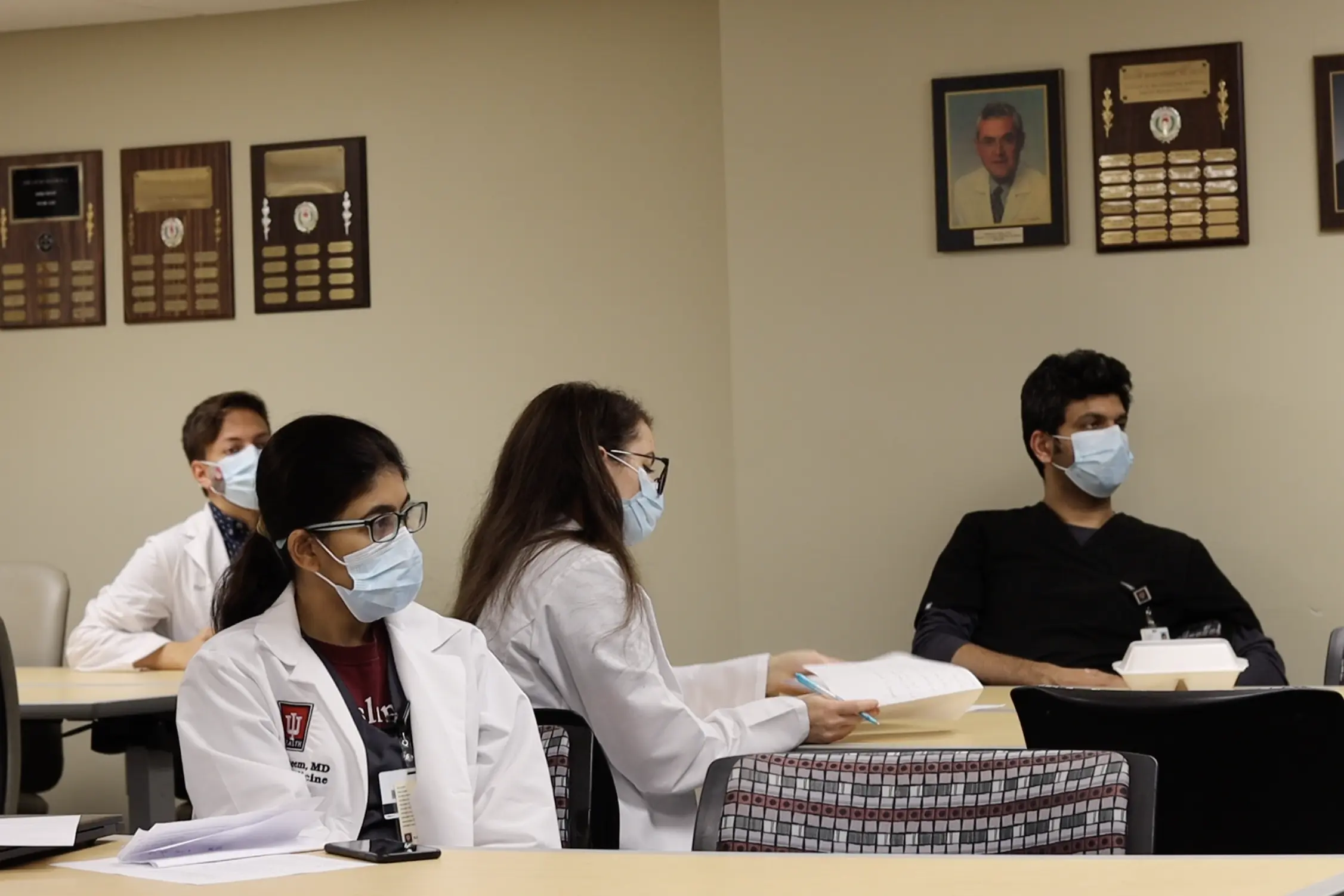 residents sit together in a conference room wearing white coats and masks