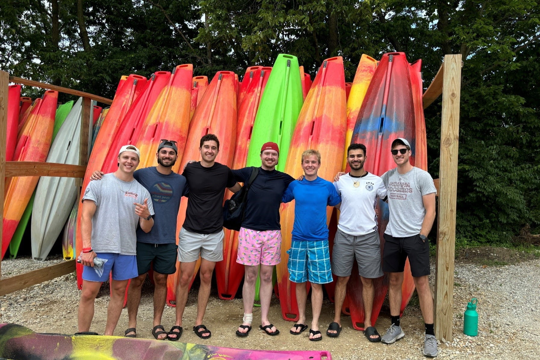 seven residents stand arm in arm in front of a large rack of colorful kayaks