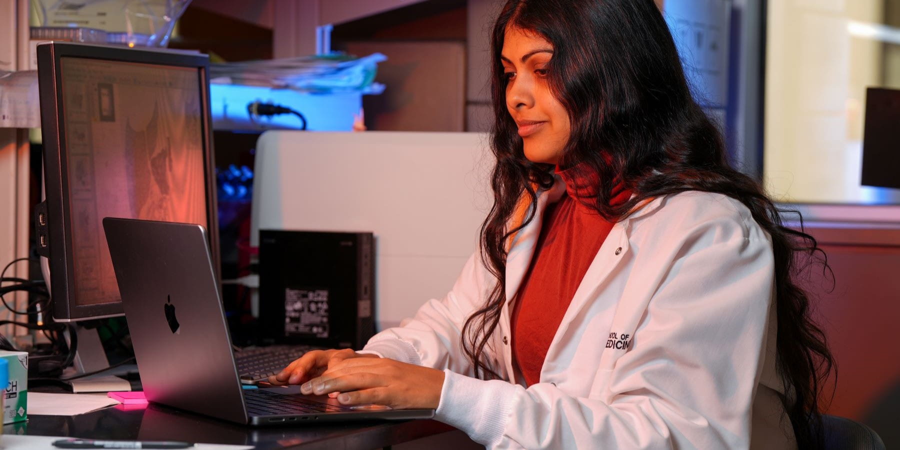 a graduate student sits in the lab working on a laptop