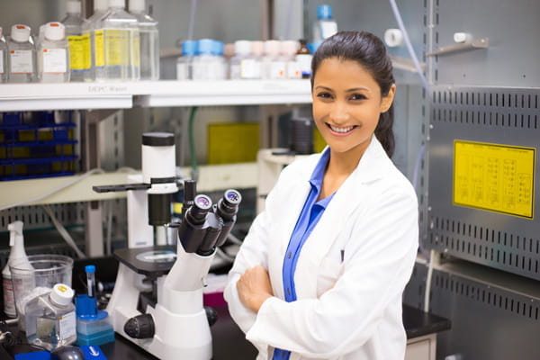 a young female histotechnician wearing a lab coat stands in front of a microscope.