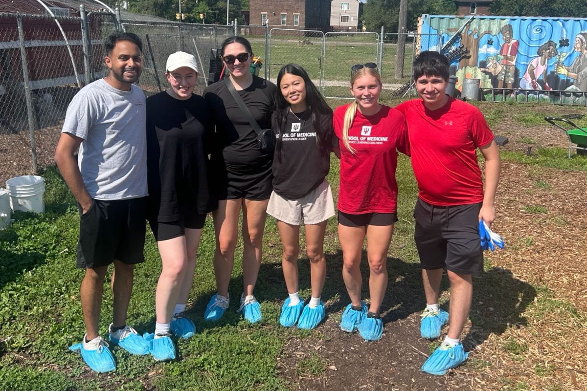 A group of IU medical students wearing shoe protectors in a field as they prepare to work in a day of service to the Faith Farms organization.