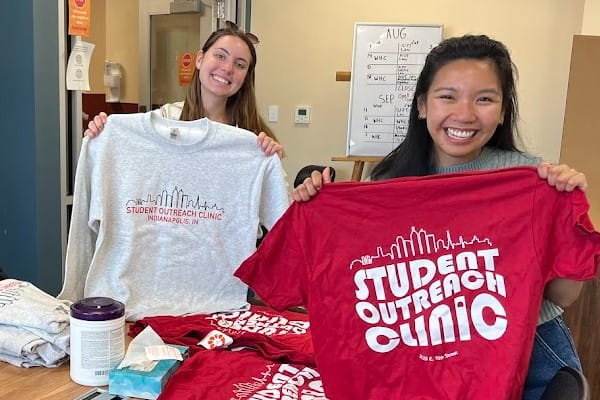 Two IU School of Medicine students working for the Indianapolis Student Outreach Clinic hold up their shirts showing their pride for the program.