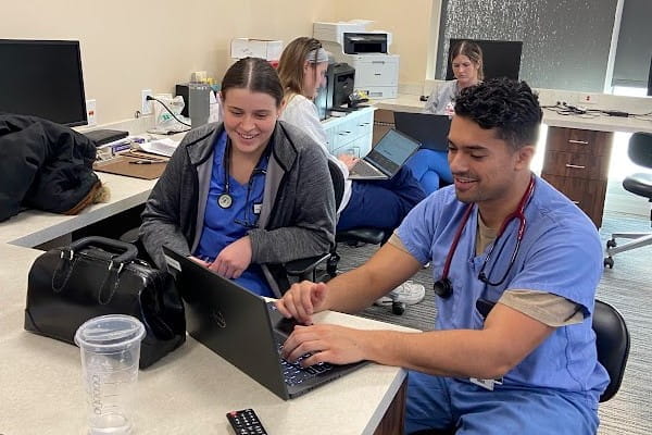 two IU School of Medicine students in scrubs sit in front of a laptop working diligently