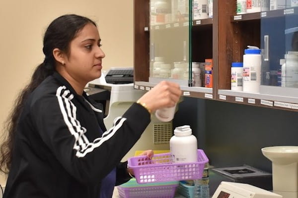 A student working at the Indianapolis Student Outreach Clinic grabs different bottles of medicine from a cabinet.
