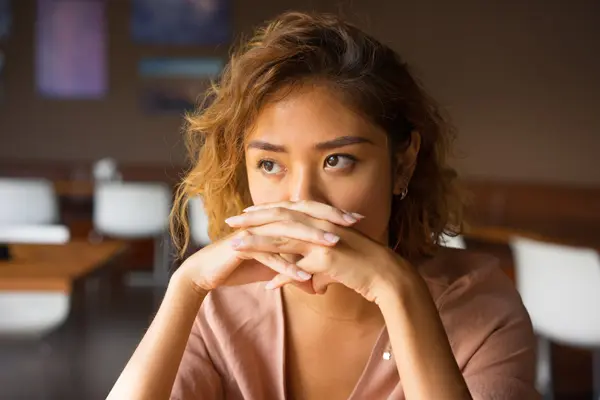 a serious young woman covers her mouth with clasped hands