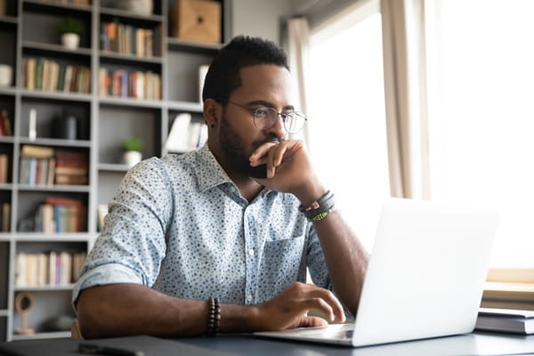 a Black man sits thoughtfully at a computer