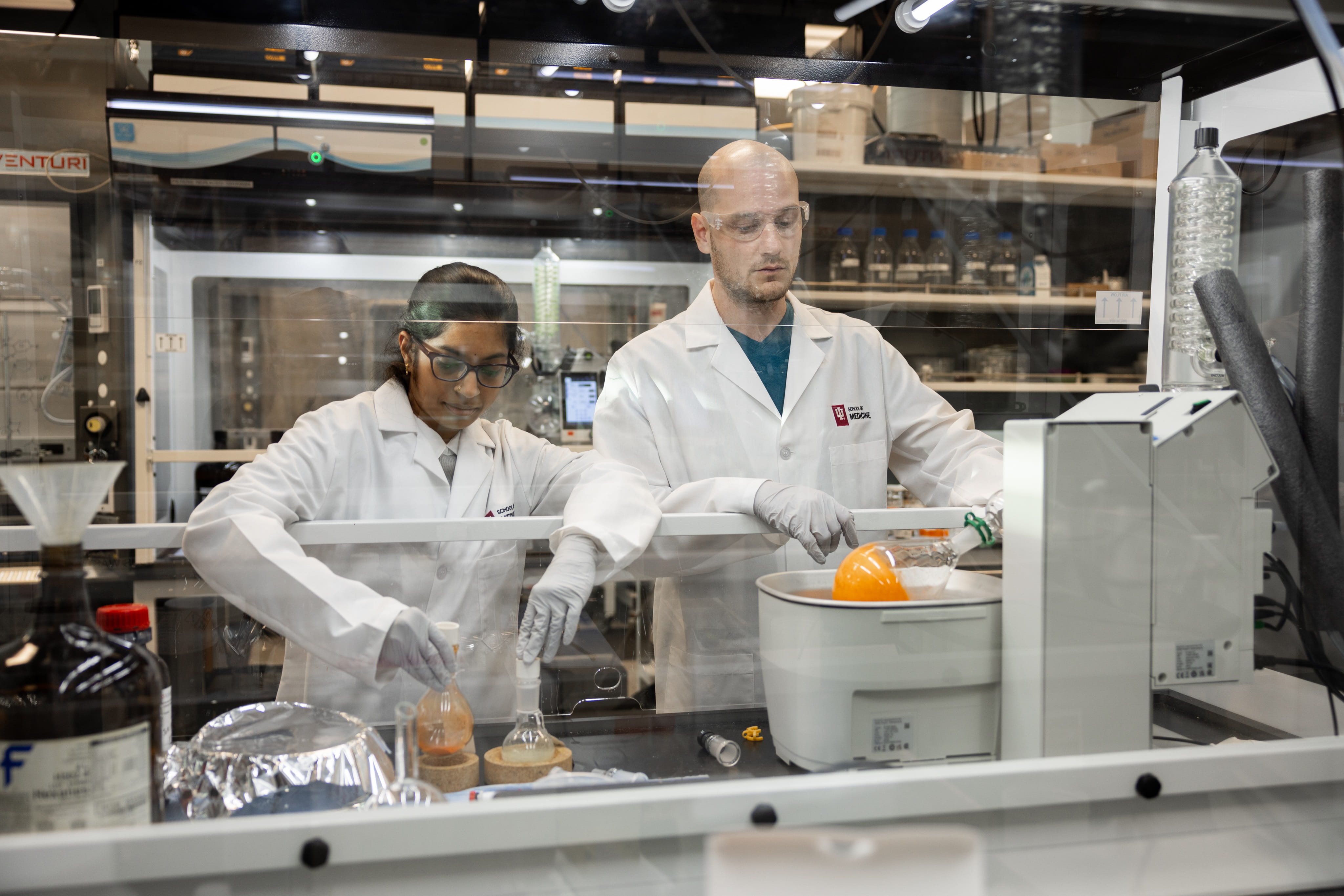 two scientists work behind glass in a lab