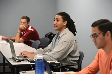 three students listen and take notes in class