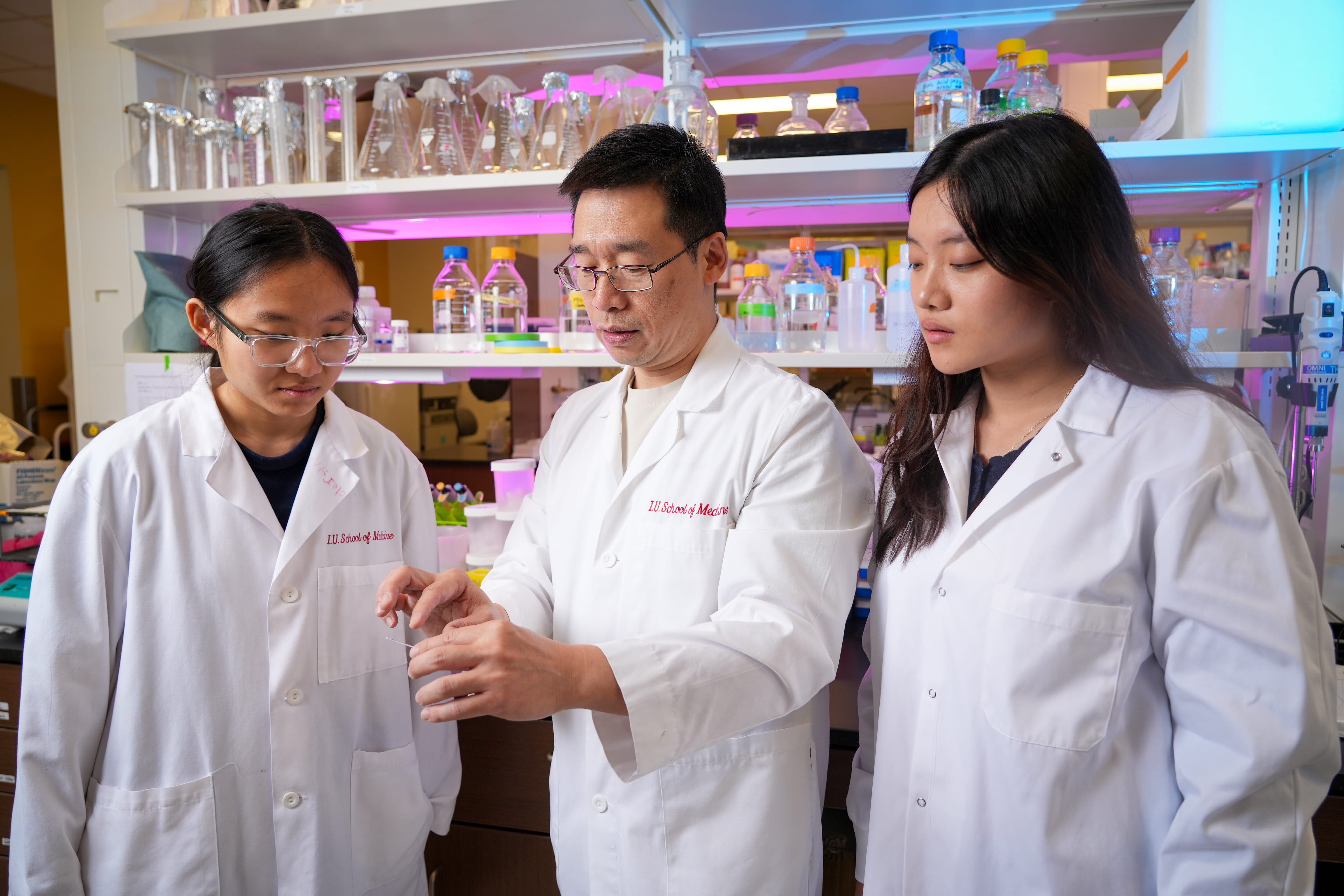 Dr. Deng with students looking at a microscope slide