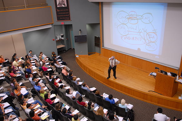 An audience listens to a lecturer on stage at IU School of Medicine