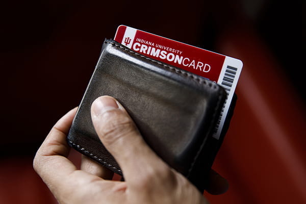 A hand is holding a wallet with a Crimson Card partially sticking out of it.