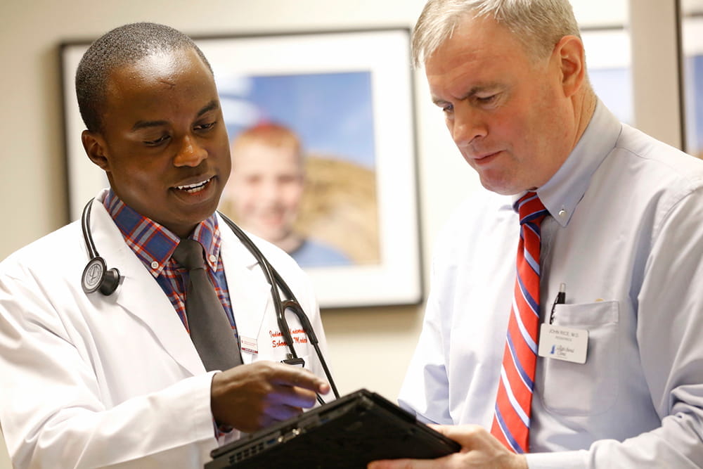 Two colleagues review and discuss a patient chart in a hallway.