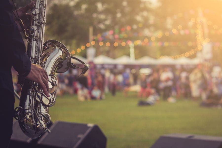from behind the stage, someone plays the saxophone as a crowd of people at the concert sit in the background